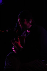 Robin Pecknold, seated, singing while playing guitar on stage