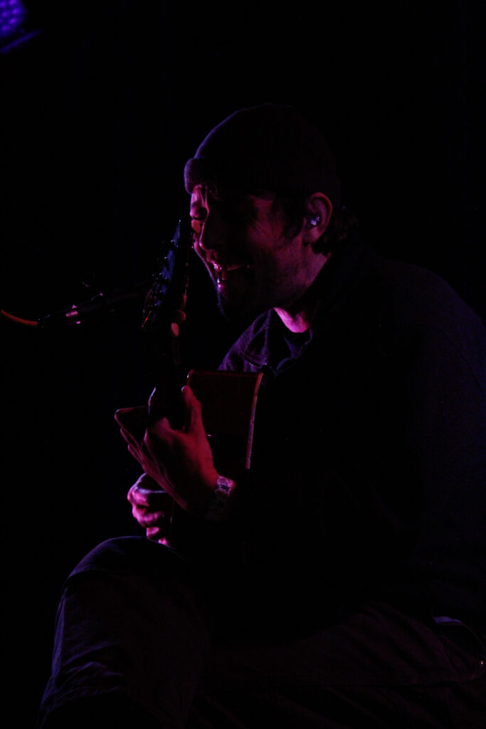 Robin Pecknold, seated, singing while playing guitar on stage