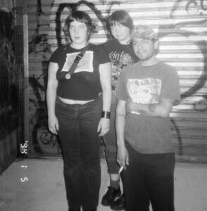 Black and white photo of rock trio Pocket Full of Crumbs in front of a graffiti strewn wall