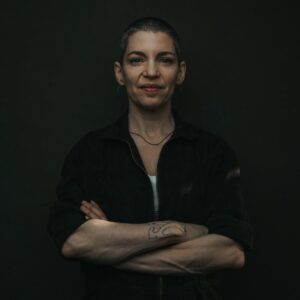 Carla Kihlstedt standing in a dark room with her arms folded.