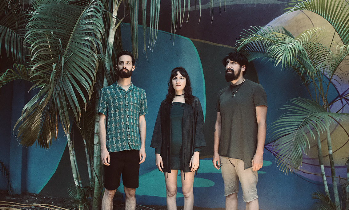 Three band members of Karen Y Los Remedios standing in front of a wall of tropical plant images