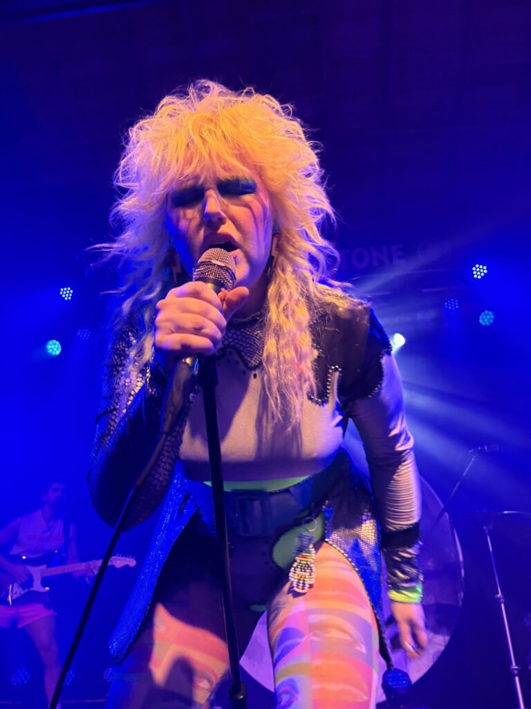 Caroline Kingsbury bent at the hips singing looking into the crowd