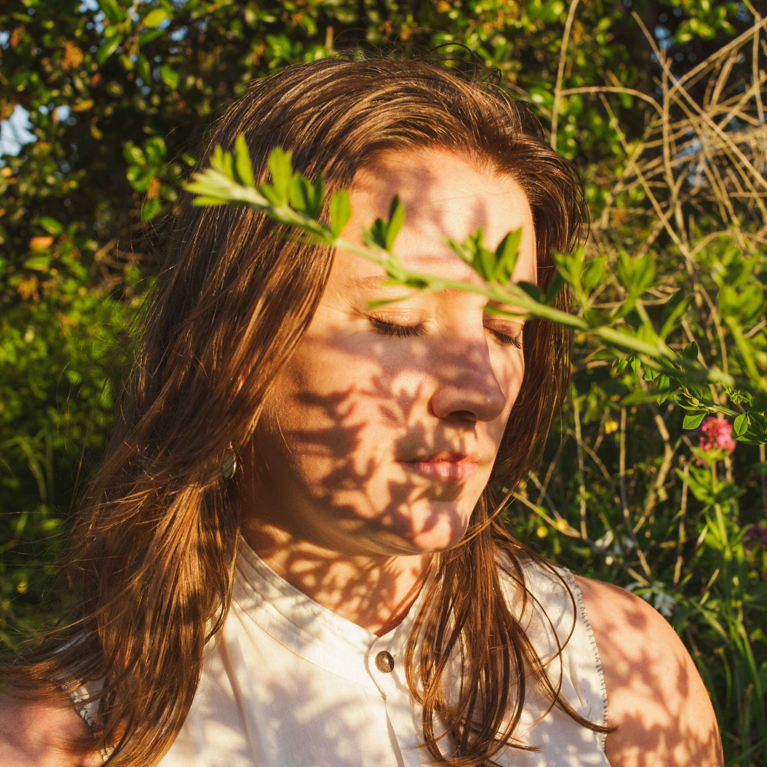 Lizzy Dutton, eyes closed, standing amongst greenery in the sun